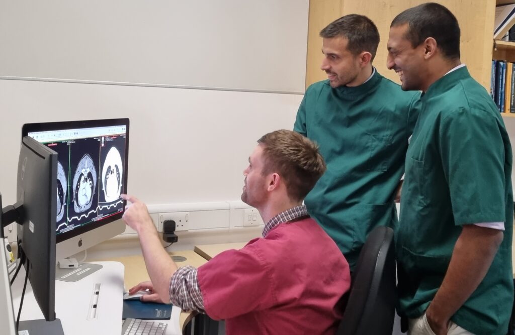 An image of three men in veterinary scrubs looking at a scan of a heart on a computer screen. 